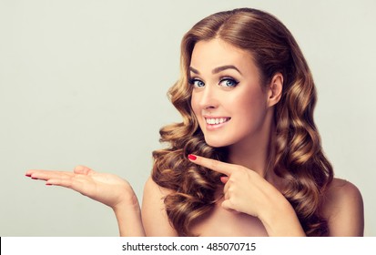 Woman surprise showing product .Beautiful girl with curly hair pointing to the side . Presenting your product. Expressive facial expressions  - Powered by Shutterstock