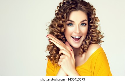 Woman surprise showing product with cunning look .Beautiful girl with curly hair looking away . Presenting your offer. Isolated on white background. Expressive facial expressions
