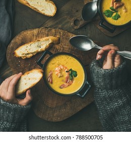 Woman In Sweater Eating Corn Creamy Soup With Shrimps In Individual Pot, Top View, Square Crop. Woman' S Hand With Spoon And Bread. Flat-lay Of Rustic Table. Slow Food, Winter Warming Food Concept