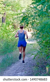 Woman With Sweaty Back In Blue Sportswear Runs Along Dirt Road In Forest