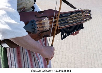 Woman in Swedish traditional costume plays folk music on a Swedish nyckelharpa in a close-up with focus on the bow, strings and bridge