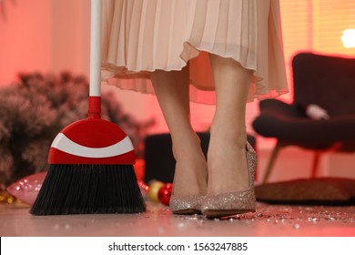 Woman With Sweep Broom Cleaning Messy Room After New Year Party, Closeup Of Legs