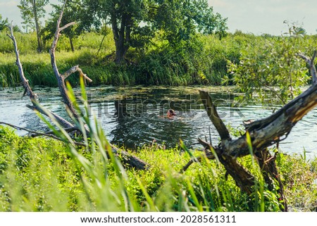 woman is swimming on a river with banks overgrown with grass. Leisure activity