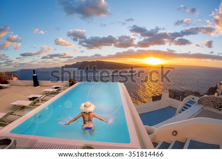 Woman in the swimming pool against sunset in Oia village on Santorini island, Greece