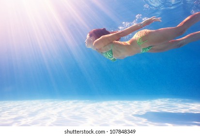 Woman swimming underwater in a blue pool.