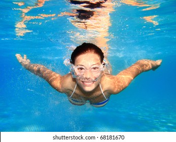 Woman swimming underwater in pool smiling. Young female swimmer with swim goggles at holiday resort.