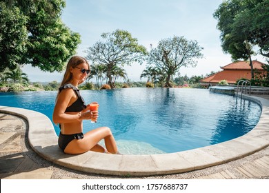 Woman swims to the edge of swimming pool, takes fresh juice, drinks it and swims away, sunny day in the swimming pool outdoors, relaxing in the pool - Powered by Shutterstock