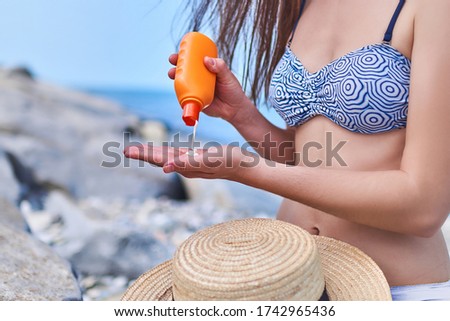Woman in a swimsuit apply sunscreen cream during sunbathing by the sea in sunny hot weather in the summer