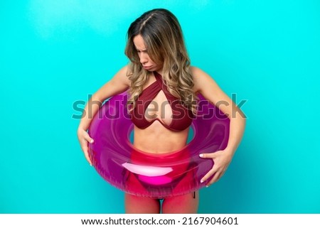 Woman in swimsuit holding floater isolated on blue background with sad expression