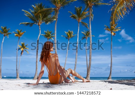 Woman in a swimsuit. Sitting on the ocean and high palm trees                              