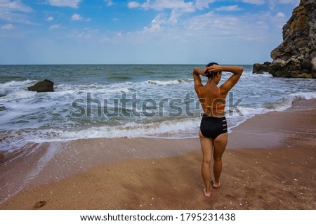 Woman in a swimsuit standing on the seashore, back view