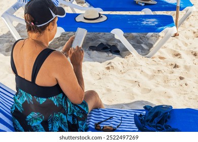 Woman in swimsuit using smartphone while relaxing on sandy beach near blue sun loungers. Miami Beach. USA.  - Powered by Shutterstock