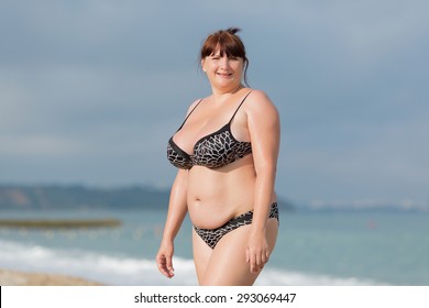 Woman in swimwear at the sea. Overweight young woman in swimsuit against the sea. She looking at camera smiling
