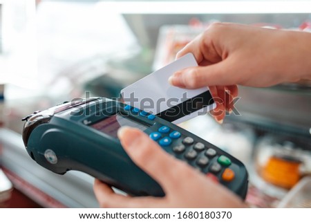 The woman swipes a Bank card through the payment machine to complete the purchase payment. Hands close-up. NFC concept, business and banking operations