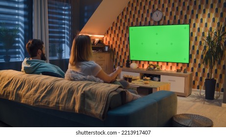 Woman switching channels with remote control. Couple sitting on couch in living room, talking, watching breaking news, movie or series on TV. Resting at home in the evening. Green screen. Chromakey. - Powered by Shutterstock