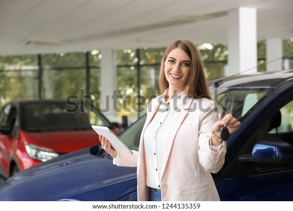 Woman\
with tablet and car keys in modern auto\
dealership