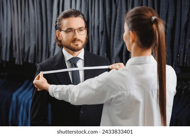 Woman tailor taking measurements of young handsome man, fitting bespoke suit to model. Lux Atelier Classic Menswear. - Powered by Shutterstock