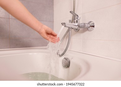 Woman Take Bath At Home Checking Temperature Touching Running Water With Hand. Fingers Under Hot Water Out Of A Faucet Of A Sink Or Bathtub In House Bathroom