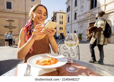 Woman Take Photo Of Italian Pasta At Restaurant On The Street In Rome. Concept Of Italian Gastronomy And Food Blogging. Stylish Woman In Dress With Colorful Hair Shawl