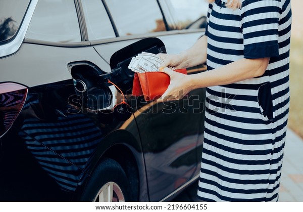 woman takes money dollars out of\
her wallet while standing next to a car with an open fuel\
tank