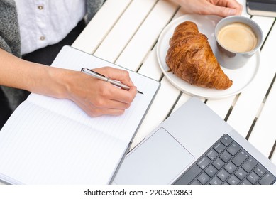 A Woman Takes Notes And Has Breakfast In Front Of A Laptop During An Online Business Meeting.