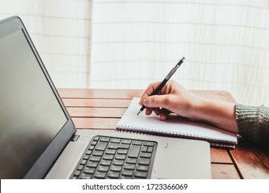 A woman takes notes on a paper next to a laptop. Concept of work from home during quarantine. - Shutterstock ID 1723366069