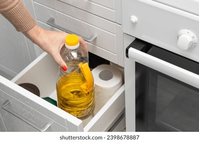 Una mujer saca una botella de aceite de girasol de un cajón. mano sujetando una botella de aceite. freír petróleo. aceite de cocina.  