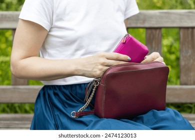 woman takes out a wallet from a lady's handbag. woman's hand takes out a wallet from a bag. woman in the park with a handbag. leather wallet. woman in a skirt. 