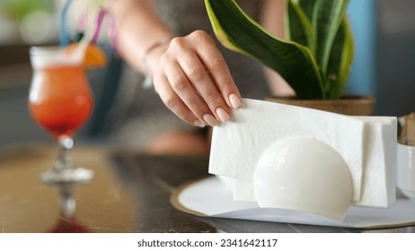 Woman takes paper napkin from ceramic napkin holder on served table