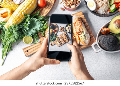 A woman takes a photo of spring rolls on her smartphone. - Powered by Shutterstock