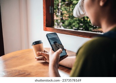 A woman takes a picture of a paper coffee cup in hand with her smartphone while sitting at a coffee shop. - Powered by Shutterstock