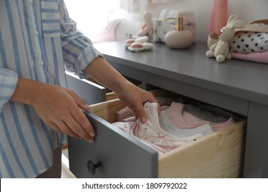 Woman Taking Baby Clothes From Open Cabinet Drawer In Child Room, Closeup