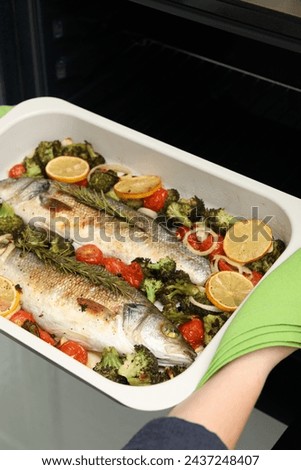 Woman taking baking dish with delicious fish and vegetables from oven, closeup