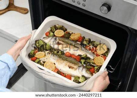 Woman taking baking dish with delicious fish and vegetables from oven in kitchen, closeup