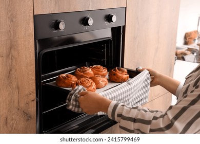 Woman taking baking tray with buns from oven in kitchen, closeup