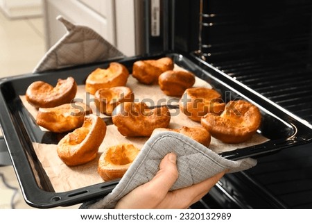 Woman taking baking tray with tasty Yorkshire pudding out from oven in kitchen