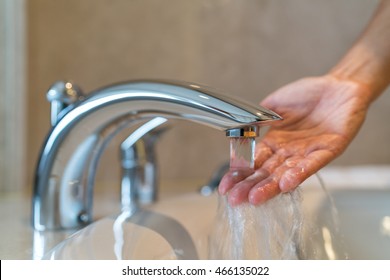 Woman Taking A Bath At Home Checking Temperature Touching Running Water With Hand. Closeup On Fingers Under Hot Water Out Of A Faucet Of A Sink Or Bathtub In House Bathroom