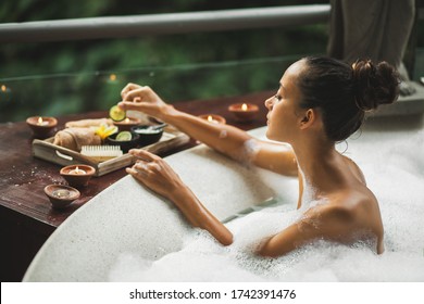 Woman Taking A Bath. Tub With Foam Bubbles. Romantic Spa Treatment, Body Care. Natural Cosmetics Set On Wooden Tray.