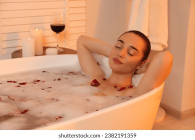 Woman taking bath in tub with foam and rose petals indoors - Powered by Shutterstock