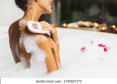 Woman taking a bath and washing with natural jute sponge. Tub with foam bubbles. View from behind. Spa treatment, body care. Leisure time. - Powered by Shutterstock