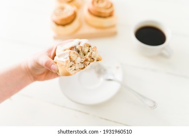 Woman Taking A Bite Out Of A Delicious Cinnamon Roll. Caucasian Woman With Sugar Cravings Eating A Sweet Pastry For Dessert With A Cup Of Coffee At The Kitchen Table