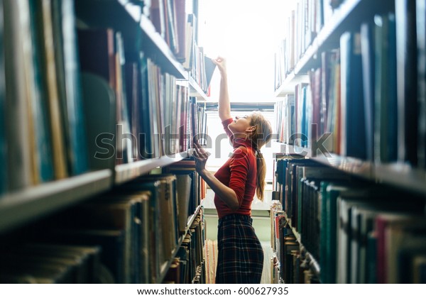 Woman taking\
book from library bookshelf. Young librarian searching books and\
taking one book from library\
bookshelf