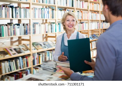 Woman Taking Book In Book Shop And Talking To Seller