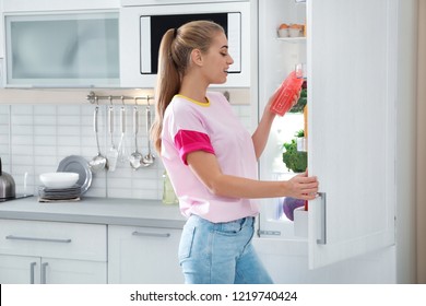 Woman Taking Bottle Of Juice Out Of Refrigerator In Kitchen