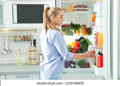Frauen, die eine Flasche mit Milch aus dem Kühlschrank in der Küche nehmen