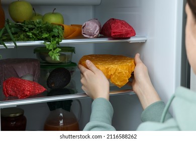 Woman taking bowl covered with beeswax food wrap from refrigerator, closeup