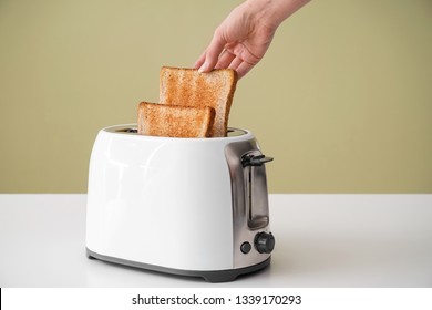 Woman Taking Bread Slice From Toaster On Table