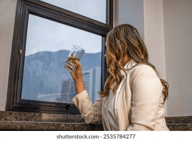 Woman Taking a Break at Work, Looking Out Rainy Window with Empty Glass - Powered by Shutterstock