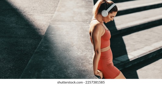 Woman taking a breather after a run outdoors. Sporty woman doing a cardio workout in the morning. Female jogger wearing wireless headphones and sportswear. - Powered by Shutterstock