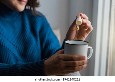 Woman taking Cannabis cbd oil inside tea cup - Alternative medicine, vitamins and supplements concept - Focus on dropper